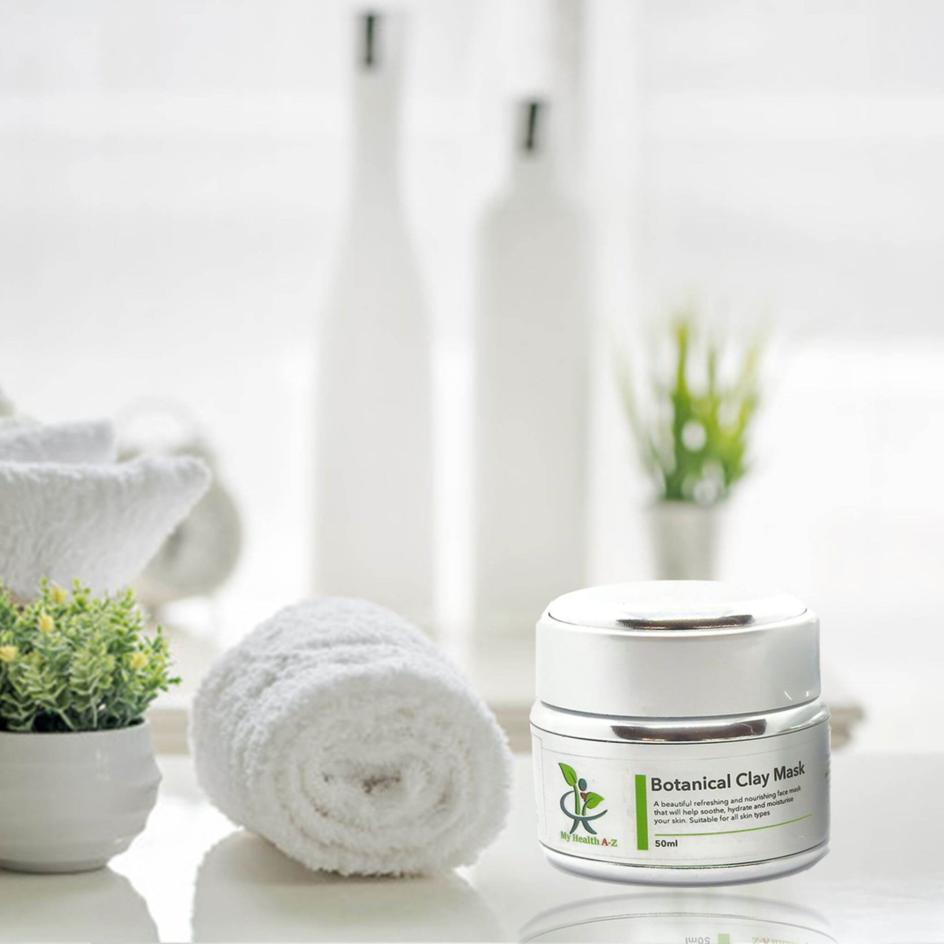 Botanical Clay Mask jar on a white surface with towels and plants in the background