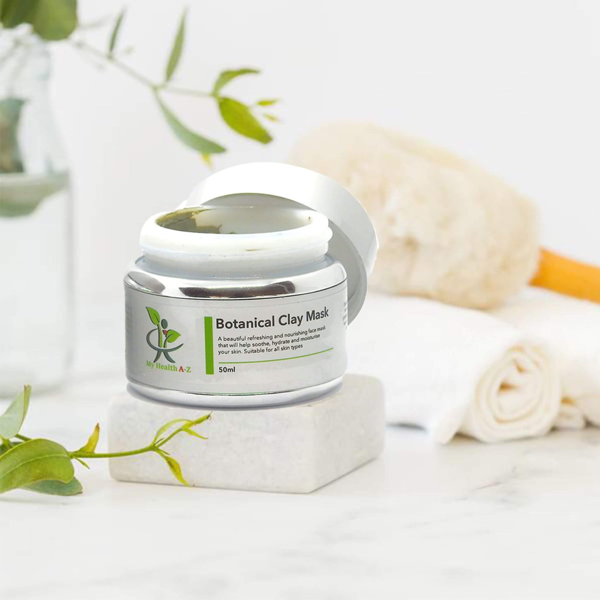 Botanical Clay Mask jar with green leaves and towel in the background
