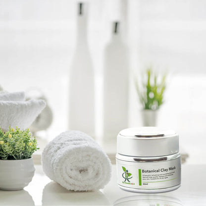 Botanical Clay Mask jar on a white surface with towels and plants in the background