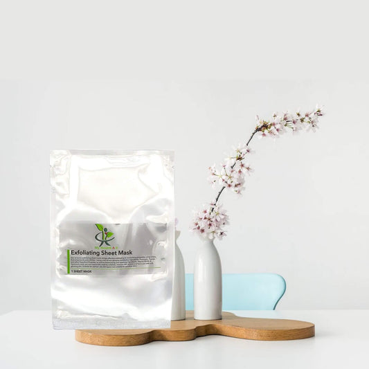 Exfoliating sheet mask packaging on a white surface with a vase and branch in the background